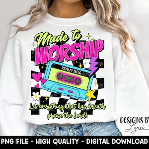 May include: White sweatshirt with a colorful graphic design. The design includes the words "Made to WORSHIP" in a retro font, a cassette tape, and the text "Let everything that has breath praise the Lord!" The design also includes a lightning bolt, stars, hearts, and a flower.