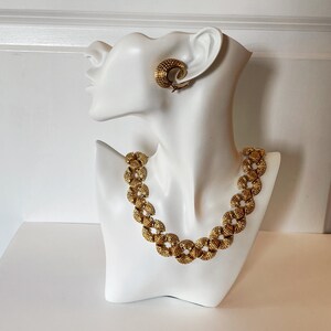May include: A gold-tone necklace and earrings set with a textured, circular design. The necklace is made of linked circles and the earrings are hoop-shaped.