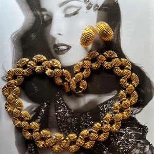 May include: A gold necklace and earrings set with a textured, circular design. The necklace is made of linked circles and the earrings are hoop-shaped.