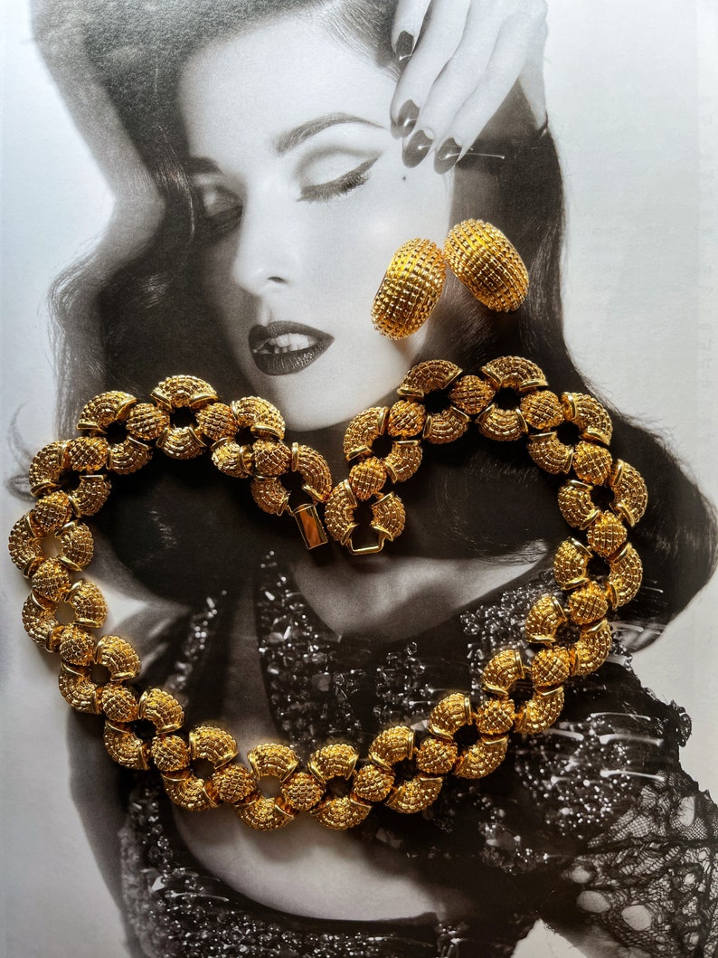 May include: A gold necklace and earrings set with a textured, circular design. The necklace is made of linked circles and the earrings are hoop-shaped.