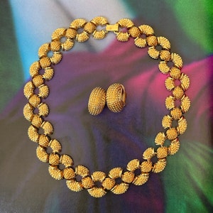 May include: A gold necklace and earrings set with a textured, circular design. The necklace is made of linked circles and the earrings are hoop-shaped.