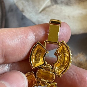May include: Gold-toned metal bracelet with a floral design and a clasp. The bracelet is made of multiple pieces that are connected together.