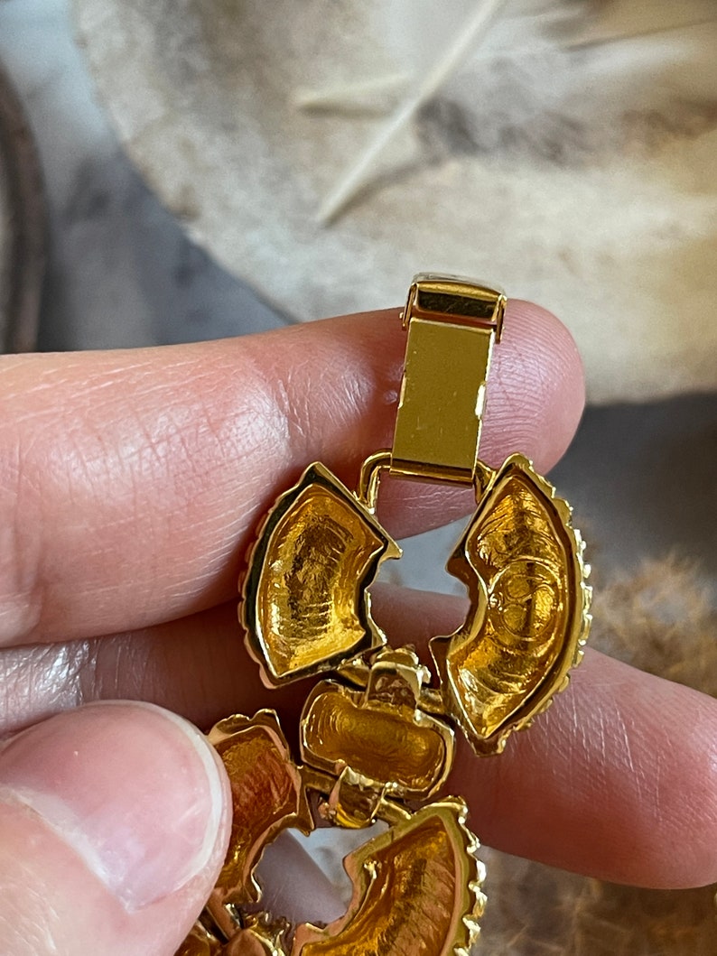 May include: Gold-toned metal bracelet with a floral design and a clasp. The bracelet is made of multiple pieces that are connected together.