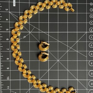 May include: A gold necklace and matching earrings with a textured, circular design. The necklace is made of small, linked circles.