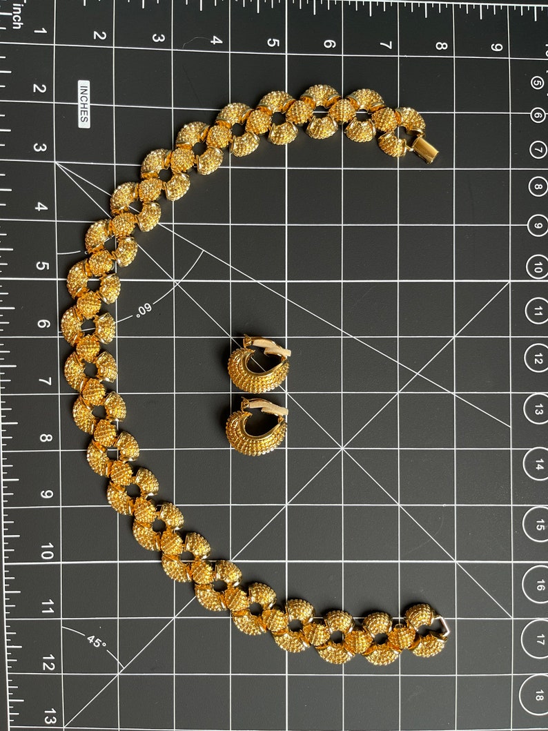 May include: A gold necklace and matching earrings with a textured, circular design. The necklace is made of small, linked circles.