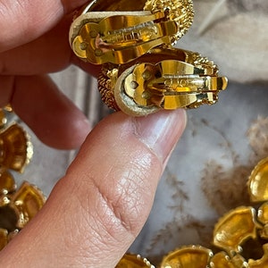 May include: A pair of gold-tone clip-on earrings with a textured design. The earrings are marked "St. John's".