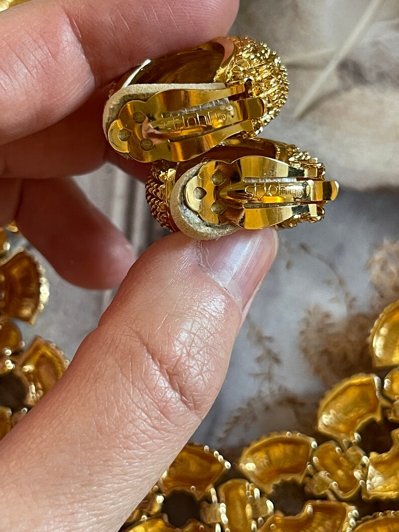 May include: A pair of gold-tone clip-on earrings with a textured design. The earrings are marked "St. John's".