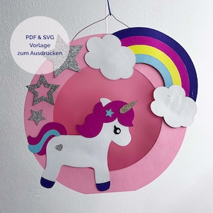 May include: A circular wall hanging featuring a white unicorn with a pink mane and tail, a gold horn, and a small heart detail. The design includes a colourful rainbow, white clouds, and silver glitter stars on a pink background with text.