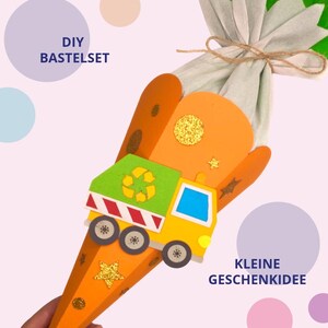 May include: An orange cone-shaped gift container featuring a yellow and green garbage truck cutout with a recycling symbol, decorated with gold glitter stars and circles, topped with light green fabric tied with twine, and text reading DIY BASTELSET.