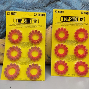Peut inclure: Deux cartes jaunes avec l'inscription "TOP SHOT 12" et "72 SHOT". Chaque carte contient six amorces en forme d'anneaux rouges. Le texte "MADE IN ITALY" est également visible.