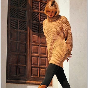 May include: A woman wearing a long, brown, knitted sweater dress with black leggings and brown cowboy boots. She is standing in front of a wooden door with a patterned design.