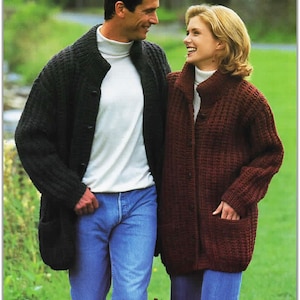 Puede incluir: Una pareja lleva cárdigans de punto. El hombre lleva un cárdigan gris oscuro con una camisa de cuello alto blanca y pantalones vaqueros azules. La mujer lleva un cárdigan burdeos con una camisa de cuello alto blanca y pantalones vaqueros azules.