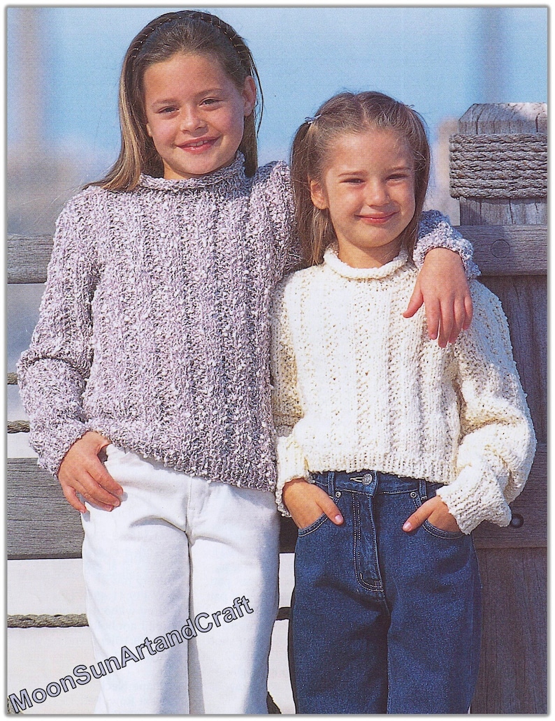 May include: Two girls wearing knitted sweaters. The girl on the left is wearing a light purple sweater and white pants. The girl on the right is wearing a white sweater and blue jeans.