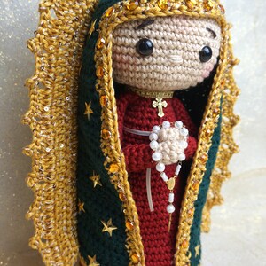 Puede incluir: Figurita de ganchillo de la Virgen Mar&iacute;a, vestida con una t&uacute;nica azul y roja con ribetes dorados y una corona. Lleva un rosario en sus manos.