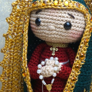 Puede incluir: Mu&ntilde;eca de crochet de la Virgen Mar&iacute;a con un vestido rojo, una corona dorada y un collar dorado con una cruz. Ella sostiene un rosario blanco en sus manos.