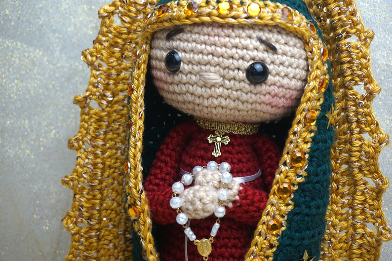 Puede incluir: Mu&ntilde;eca de crochet de la Virgen Mar&iacute;a con un vestido rojo, una corona dorada y un collar dorado con una cruz. Ella sostiene un rosario blanco en sus manos.