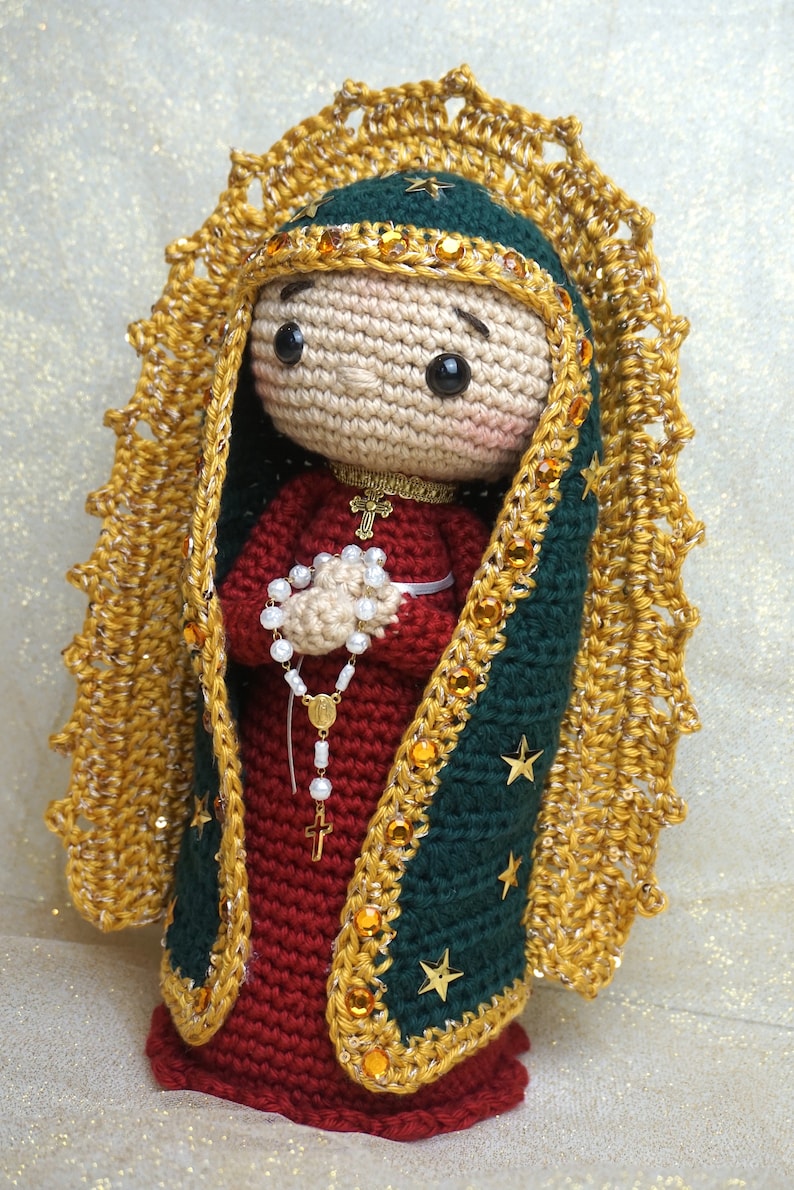 Puede incluir: Figurita de ganchillo de la Virgen Mar&iacute;a, vestida con una t&uacute;nica azul y dorada con una corona de oro y estrellas. Ella sostiene un rosario en sus manos.