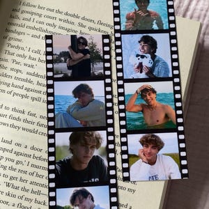 Peut inclure: Marque-page en forme de bande de film avec six petites photos d'une personne. Le marque-page est pos&eacute; sur un livre ouvert avec du texte imprim&eacute;.