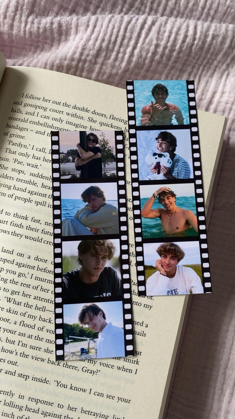 Peut inclure: Marque-page en forme de bande de film avec six petites photos d'une personne. Le marque-page est pos&eacute; sur un livre ouvert avec du texte imprim&eacute;.