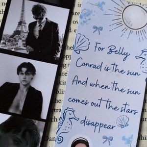 Puede incluir: Un marcap&aacute;ginas con un fondo azul claro con una ilustraci&oacute;n de un sol, una concha y un caballito de mar. El texto dice: "Para Belly Conrad es el sol Y cuando el sol sale, las estrellas desaparecen". Incluye una ilustraci&oacute;n de pareja.
