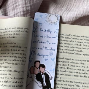 Puede incluir: Marcap&aacute;ginas azul claro con el texto "For Belly Conrad is the sun And when the sun comes out the stars disappear." El marcap&aacute;ginas presenta una pareja con ropa formal y elementos decorativos.