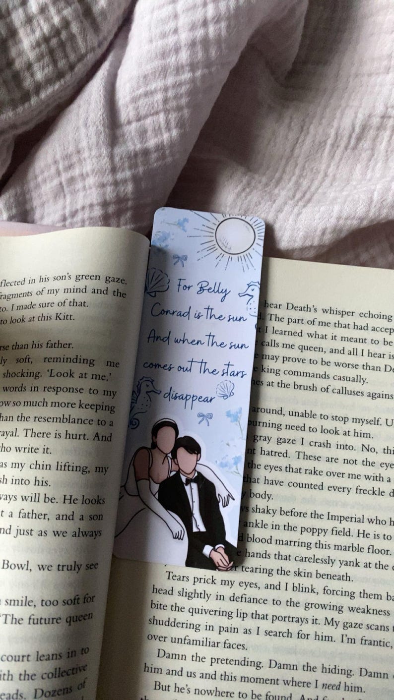 Puede incluir: Marcap&aacute;ginas azul claro con el texto "For Belly Conrad is the sun And when the sun comes out the stars disappear." El marcap&aacute;ginas presenta una pareja con ropa formal y elementos decorativos.