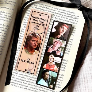 May include: A bookmark with a photo of a young man, the text reads "Stupid Things Have Good Outcomes all The Time" and "JJ Maybank". The bookmark is in an open book, with a black ribbon.