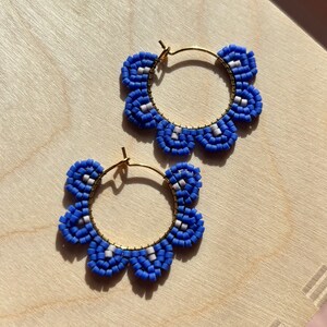 May include: A pair of blue and white beaded hoop earrings with a flower-shaped design. The earrings are made with small, round beads and have a gold-toned hoop.