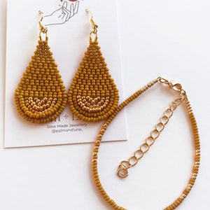 May include: A set of mustard yellow beaded earrings and a matching bracelet. The earrings are teardrop shaped and have a gold accent. The bracelet is a simple chain with a gold clasp.