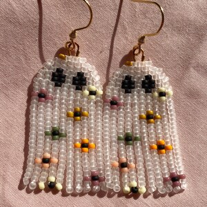 May include: A pair of beaded earrings with a fringe design. The earrings are made with white beads and feature small colorful beads in a floral pattern.