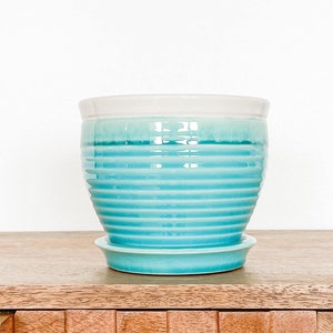 May include: A light blue ceramic planter with a white rim and a ribbed design. The planter has a matching saucer.