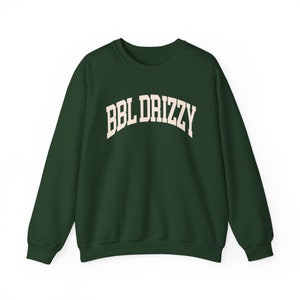 Op de afbeelding: Een donkergroen sweatshirt met de tekst "BBL DRIZZY" in een crèmekleurige, gebogen lettertype.