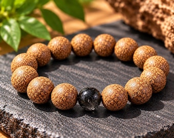 Puede incluir: Una pulsera de cuentas que presenta numerosas cuentas de madera marrón redondas y texturizadas con un patrón moteado y una cuenta de piedra negra translúcida, lisa y brillante, situada cerca del centro del conjunto.