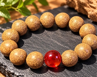 Puede incluir: Una pulsera de cuentas con catorce esferas de superficie texturizada y moteada en color marrón, junto a una esfera lisa, translúcida y de color rojo vibrante que actúa como punto focal en la disposición circular.