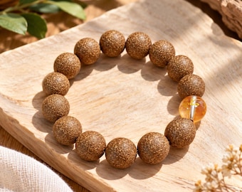 Puede incluir: Una pulsera de cuentas con numerosas cuentas redondas y texturizadas de color marrón con acabado mate, intercaladas con una sola cuenta translúcida, lisa y de color ámbar que contiene un pequeño acento metálico dorado.