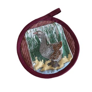 May include: A red and white checkered pot holder with a goose design. The goose is brown and gray with a white background. The pot holder has a loop handle.
