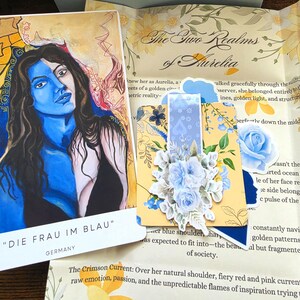 Puede incluir: Una tarjeta rectangular titulada DIE FRAU IM BLAU con el retrato de una persona con la mitad de la cara y el torso pintados de azul, junto a una tarjeta cuadrada con un arreglo floral azul y un papel impreso The Two Realms of Aurelia.