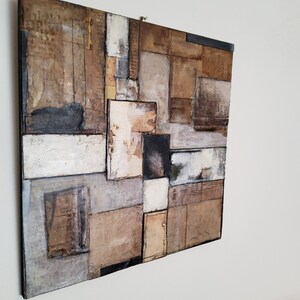 May include: Abstract art piece featuring a collage of textured paper squares in shades of brown, white, and black. The piece is framed with a black border.