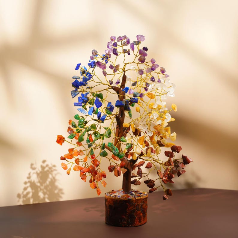 K&ouml;nnte beinhalten: Ein Kristallbaum mit sieben verschiedenen farbigen Edelsteinen, die die sieben Chakren repr&auml;sentieren, in einem braunen Topf. Der Baum ist aus Draht gefertigt und die Edelsteine sind am Draht befestigt. Der Baum steht auf einer braunen Oberfl&auml;che.