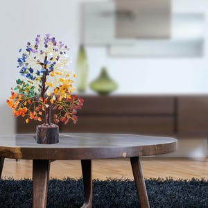 K&ouml;nnte beinhalten: Ein farbenfroher Kristallbaum mit sieben Chakra-Steinen, darunter Rot, Orange, Gelb, Gr&uuml;n, Blau, Indigo und Violett. Der Baum besteht aus Draht und hat eine Holzbasis. Er steht auf einem Holztisch.