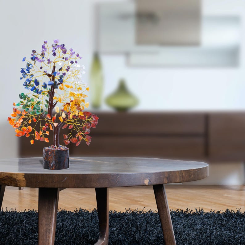 K&ouml;nnte beinhalten: Ein farbenfroher Kristallbaum mit sieben Chakra-Steinen, darunter Rot, Orange, Gelb, Gr&uuml;n, Blau, Indigo und Violett. Der Baum besteht aus Draht und hat eine Holzbasis. Er steht auf einem Holztisch.