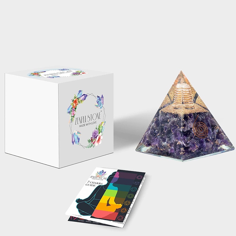 May include: Amethyst crystal pyramid with a gold metal spiral and a small golden statue inside. The pyramid is on a white surface with a white box and a 7 Chakra Guide card. The box has the text "Zenith Stone Made with Love".
