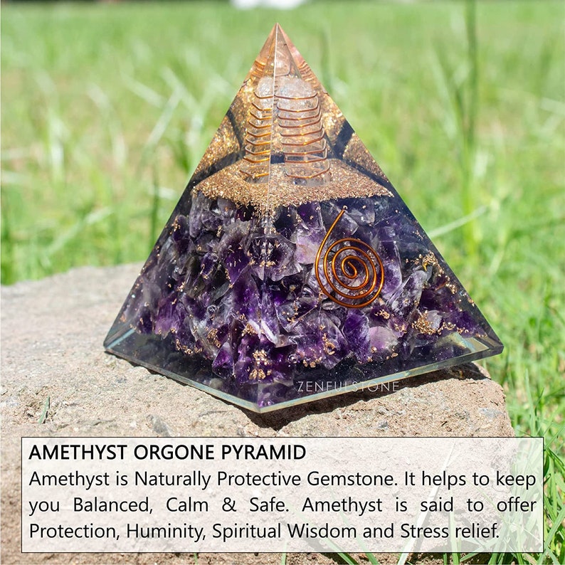 May include: Amethyst orgone pyramid with a copper coil inside. The pyramid is made of clear resin with amethyst crystals embedded in it. The pyramid is sitting on a rock with green grass in the background. ZENFULSTONE is printed on the base of the pyramid.