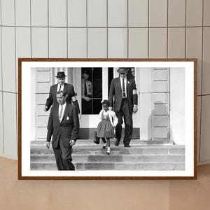May include: Black and white photograph of four people walking down a set of stairs. A young girl in a dress is walking in front of three men in suits and hats.