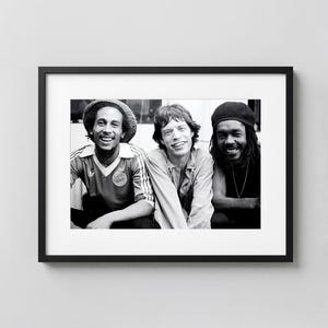 May include: Black and white framed photograph featuring three men. One man wears a soccer jersey, another a button-down shirt, and the third a black cap. All three are smiling. The photograph is displayed in a black frame.