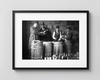 May include: Black and white photograph of a group of men in hats and suits gathered around wooden barrels and bottles. Some men are holding bottles and papers. The scene appears to be from the early 20th century.
