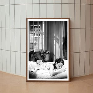 Puede incluir: Fotografía en blanco y negro de una mujer durmiendo en la cama con un gato. La mujer lleva una máscara para dormir y está tumbada de lado. El gato está acurrucado en la cama a su lado.