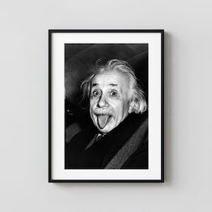 May include: A black and white framed portrait of Albert Einstein with his tongue sticking out. The photograph shows a close-up of his face, featuring his signature wild hair, mustache, and dark clothing, all encased in a simple black frame.