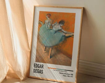 May include: A framed print of a painting by Edgar Degas titled "Dancers at the Barre" depicting two dancers in a ballet studio. The dancers are wearing pale blue tutus and are stretching at the barre. The background is a warm orange color.