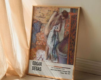 Może przedstawiać: Ramka z plakatem obrazu Edgara Degasa zatytułowanego "Après le bain (Femme s'essuyant)". Obra przedstawia kobietę w szlafroku stojącą w łazience. Plakat jest wydrukowany na białym tle z czarnym tekstem.